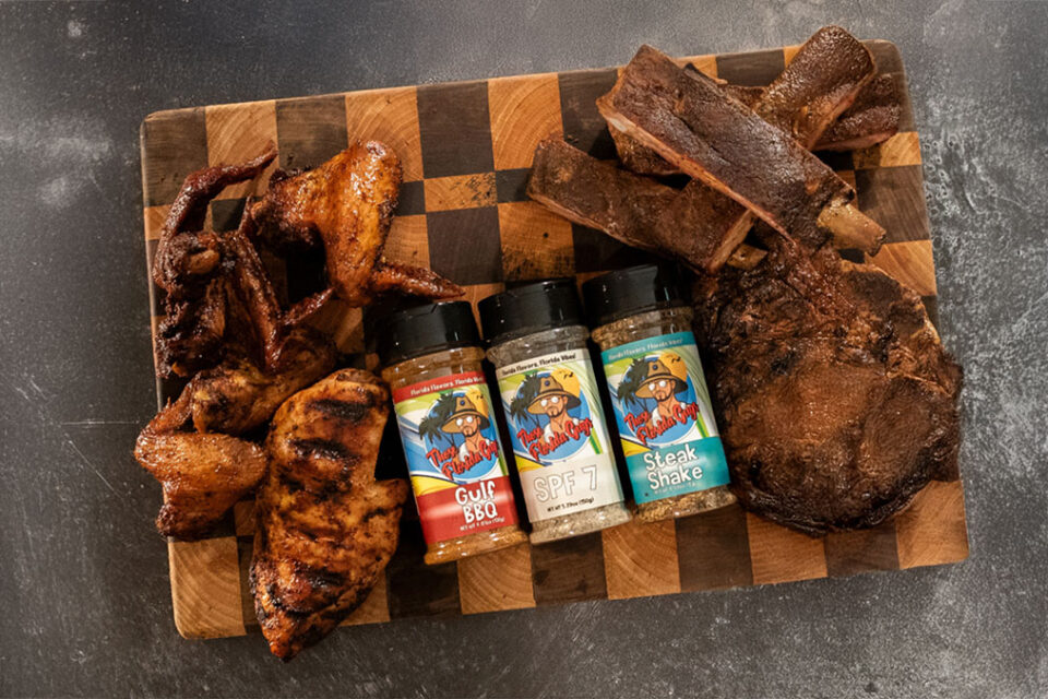 Three of Those Florida Guys BBQ rubs on top of a cutting board surrounded by pieces of meat